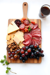 A wooden platter with assorted cheeses, cured meats, and grapes, arranged for a board. Isolated white background.