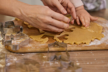 close-up, hands of mother and little child cutting cookies of raw gingerbread dough in kitchen,...