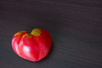Big tomato in shape of heart on brown background.