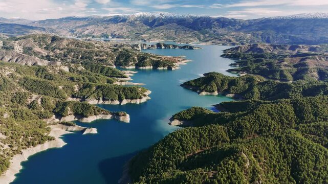 Aerial panorama revealing sinuous river winding between lush mountain slopes, snow-capped peaks framing verdant turkish wilderness landscape