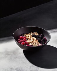 A moody smoothie bowl featuring raspberries, blackberries, granola, and almond slices, artfully styled in a black bowl with dramatic lighting.