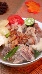 Closeup oxtail soup or sop buntut with potatoes, tomatoes, lime slices, and fried shallots. Served on a bowl white with Bamboo mat and burlap