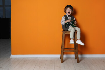 Cute little boy with old telephone on stool near orange wall, space for text