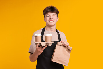 Teenage boy with order working as cashier on orange background
