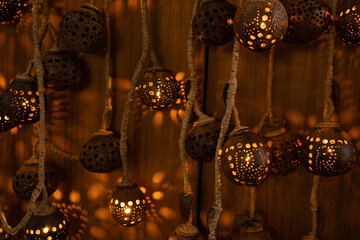 Handcrafted hanging lanterns made from natural materials with intricate perforated patterns. Warm glowing light creates decorative shadows on the wooden background, perfect for ambient designs.