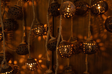 Handcrafted hanging lanterns made from natural materials with intricate perforated patterns. Warm glowing light creates decorative shadows on the wooden background, perfect for ambient designs.