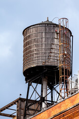 Vintage wooden water tower stands tall against a partially cloudy sky in an industrial setting.
