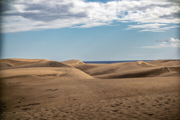 A vast desert landscape with sweeping sand dunes stretching into the distance, against a deep blue sky. The contrast between the golden sands and the rich blue sky creates a striking, serene scene