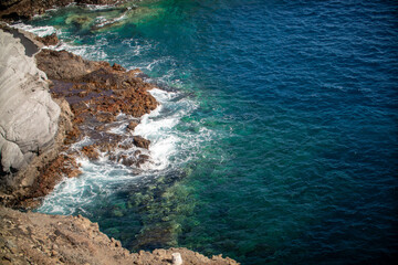 Waves from the Atlantic Ocean crashing against rugged rocks, creating a dramatic scene with splashes of white foam. The powerful ocean contrasts against the solid, jagged cliffs, under a stormy sky