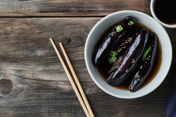 Gaji Namul a Korean side dish of steamed seasoned eggplant in a white bowl on a wooden table accompanied by soy sauce and chopsticks presented in a close up ove