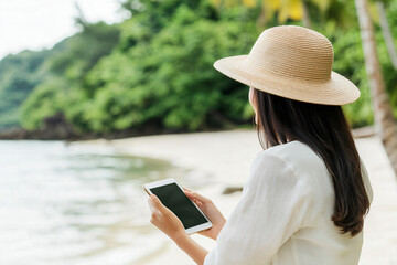 Fototapeta premium elegant businesswoman with straw hat conducting video call from paradise beach