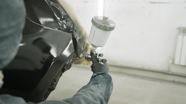 Car painter expertly applies glossy black paint to a vehicle's body, demonstrating precision and skill in auto body refinishing