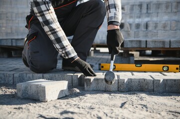 Builder laying a paving brick placing it on the sand foundation with gloved hands