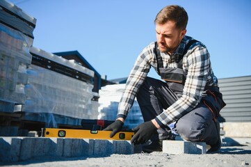 Builder laying a paving brick placing it on the sand foundation with gloved hands