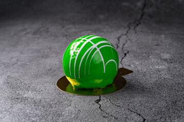 Vibrant green glazed mousse dessert with white artistic drizzle on a textured gray surface