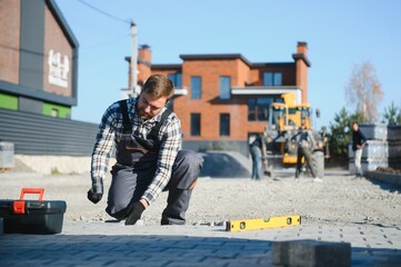 Fototapeta premium Male Worker using vibratory plate compactor to firm soil at worksite. builder. After laying of paving slabs, compacts paving stones with a gasoline vibratory compactor for subsequent