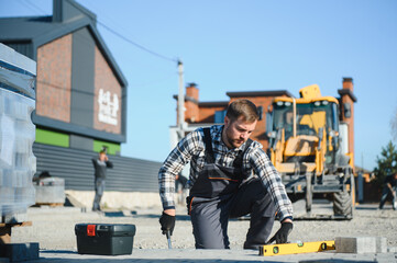 Fototapeta premium Construction worker installing and laying pavement stones on terrace, road or sidewalk. Worker using stones and rubber hammer to build stone sidewalk