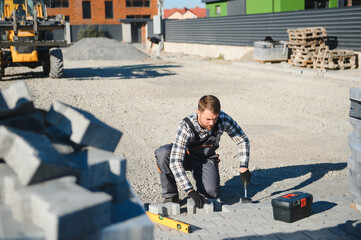 The master in gloves lays paving stones in layers. Garden brick pathway paving by professional paver worker. Laying gray concrete paving slabs in house courtyard on sand foundation base
