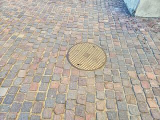 Close-up of a cobblestone street with a round manhole cover in the center. The textured surface adds character and charm to outdoor urban locations.