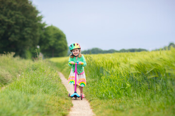 Litte girl riding scooter. Child playing outdoor.