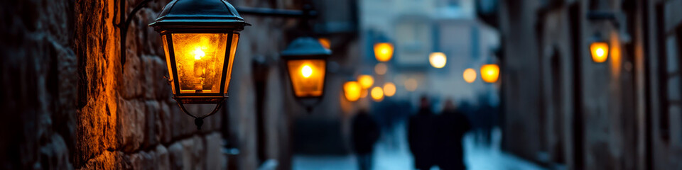 Street lamps illuminate a narrow cobblestone alley as people walk in the background. Concept of evening urban ambiance. For urban lighting theme.