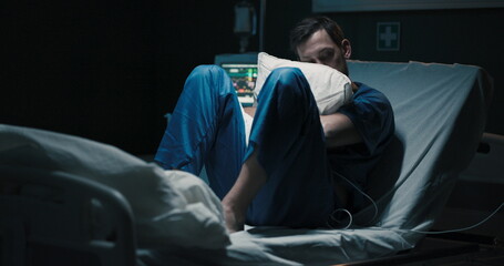 Man sits in the hospital room on the bed, hugging a pillow.