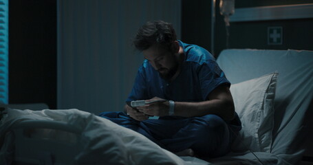Guy in hospital bed holds head, sways, seems sick.