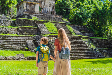 Mother and son tourists exploring the ancient pyramids of Palenque, Mexico, surrounded by dense...