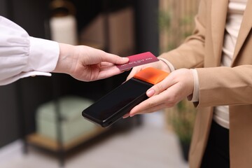 Woman paying with credit card via terminal against blurred background, closeup