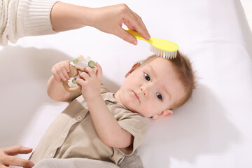 Woman brushing hair of her little baby indoors, above view