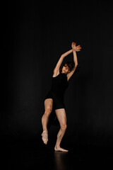 Fototapeta premium Young slim woman in black outfit with bare feet dancing in dance studio