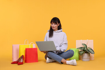 Internet shopping. Beautiful woman with laptop and colorful bags on orange background