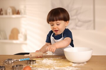 Cute little boy with rolling pin at table indoors