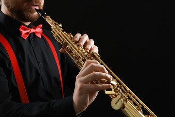 Fototapeta premium Professional musician playing soprano saxophone on black background, closeup. Space for text