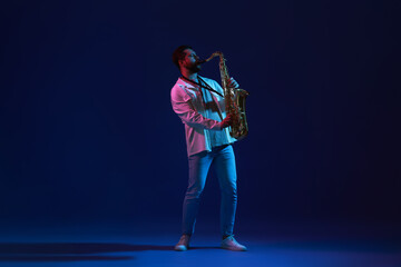 Fototapeta premium Professional musician playing saxophone on color background with neon lights