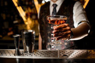 Male bartender shows off a stemmed wine glass filled with a brown cocktail