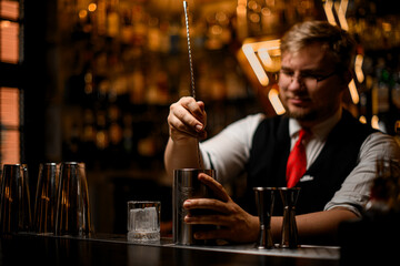 Bartender stirs a cocktail in a metal glass with a bar spoon