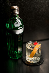 Green bottle of Tanqueray gin sits on the bar and a glass of iced drink on a coaster