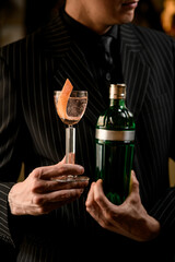 Male hands of a bartender holding a glass with a transparent drink and a piece of zest