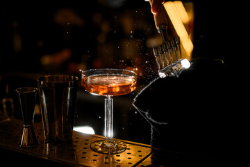 There is a goblet with a cocktail on the bar, and next to the bartender's hand, an ice cube is broken with an ice pick