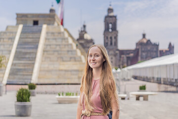 Fototapeta premium Woman tourist exploring the historic Zocalo square in Mexico City, standing in front of a replica Aztec pyramid with the Mexican flag waving in the background. The Metropolitan Cathedral can be seen
