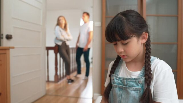 Stressed and unhappy young girl huddle in corner, cover her ears blocking sound of her parent arguing in background. Domestic violence at home and traumatic childhood develop to depression. Fastidious