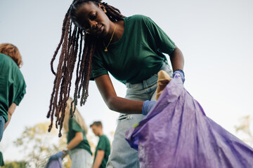 Young woman picking up trash in park with volunteers