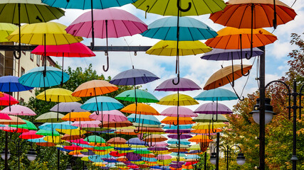 Bright installation of multicolored umbrellas suspended in the air. The cityscape gets a festive...