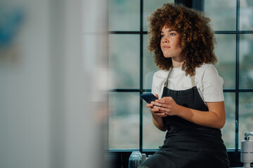 Young waitress holding smartphone and looking away in restaurant window