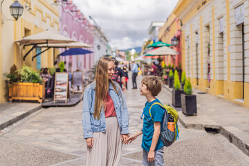 Obraz premium Mother and her son tourists walks through the colonial streets San Cristobal de las Casas, Mexico. Cultural exploration, architecture, and travel experience concept