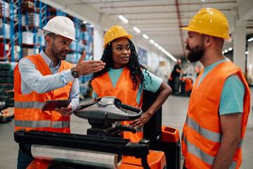 Warehouse workers discussing logistics using digital tablet and forklift