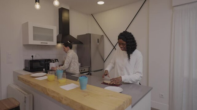 Female roommates preparing breakfast together, chopping ingredients and brewing coffee, sharing kitchen workspace with cheerful camaraderie and relaxed morning connection