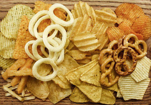 Colorful mix of salty snacks for beer varieties: chips and pretzels, onion rings and crackers. Non-healthy junk food background	