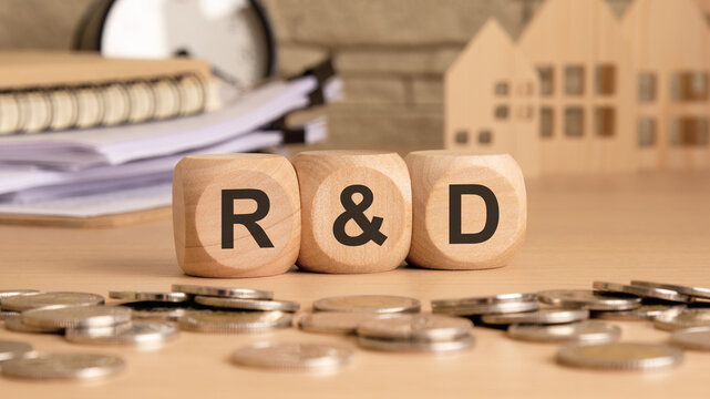 wooden blocks with R and D text, coins scattered on a desk, with documents and small house models